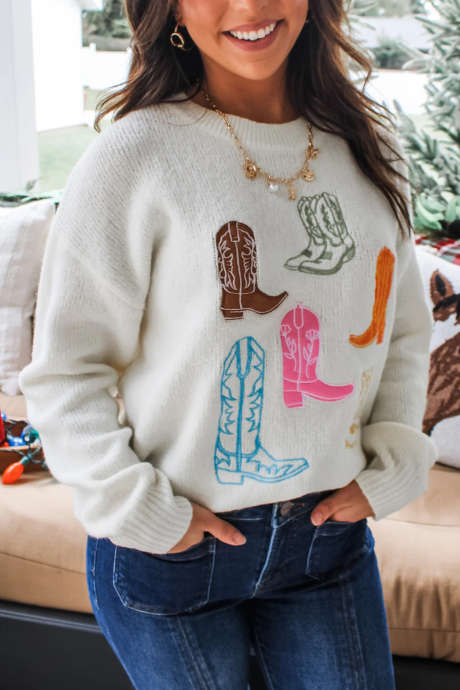 Maglione a spalle scese con ricami e motivo western bianco, stivali da cowboy.